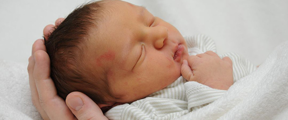 Dieses Bild zeigt ein warm zugedecktes und schlafendes Baby in den Händen einer Person.