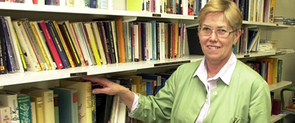 Dieses Bild zeigt ein Regal mit Büchern in der Bücherei der grünen Damen und eine Frau, die auf die Bücher hinweist.